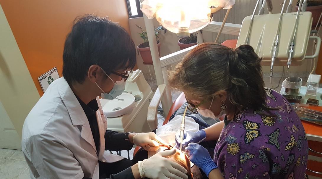 A local dentist is assisted with a dental procedure by a Japanese dentist at a clinic in Latin America.