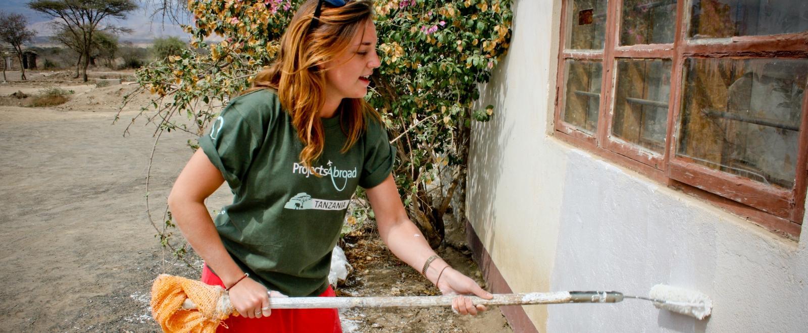 A student doing building volunteer work in Africa helps paint a newly-constructed school in Tanzania. 
