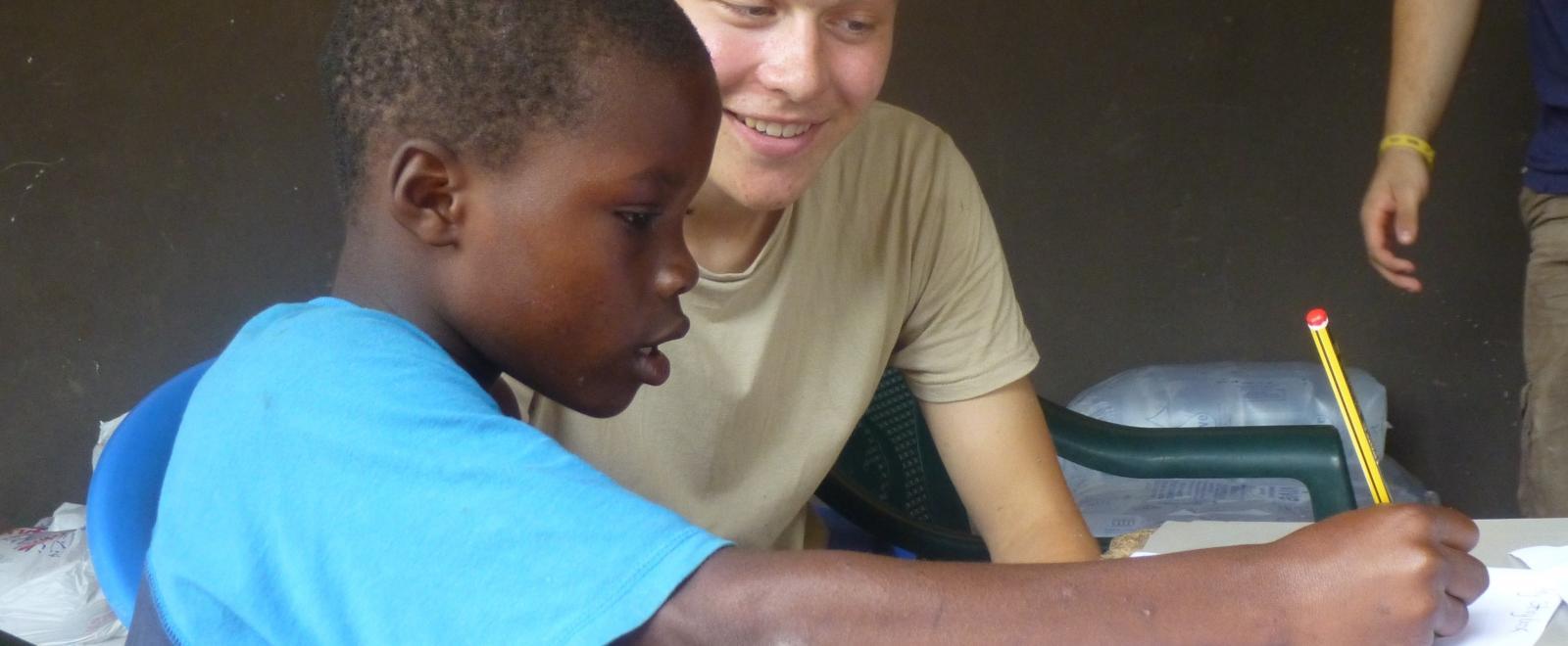 A volunteer teaching in Africa helps a child with a homework assignment at a placement in Ghana, Africa. 