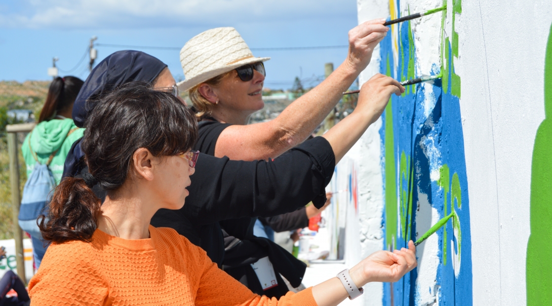 Volunteers work together to paint an educational mural while volunteering overseas on a project with no requirements.