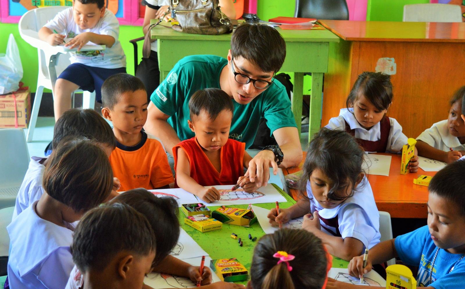A volunteer in the Philippines helps a child in the classroom as part of his service learning trip abroad