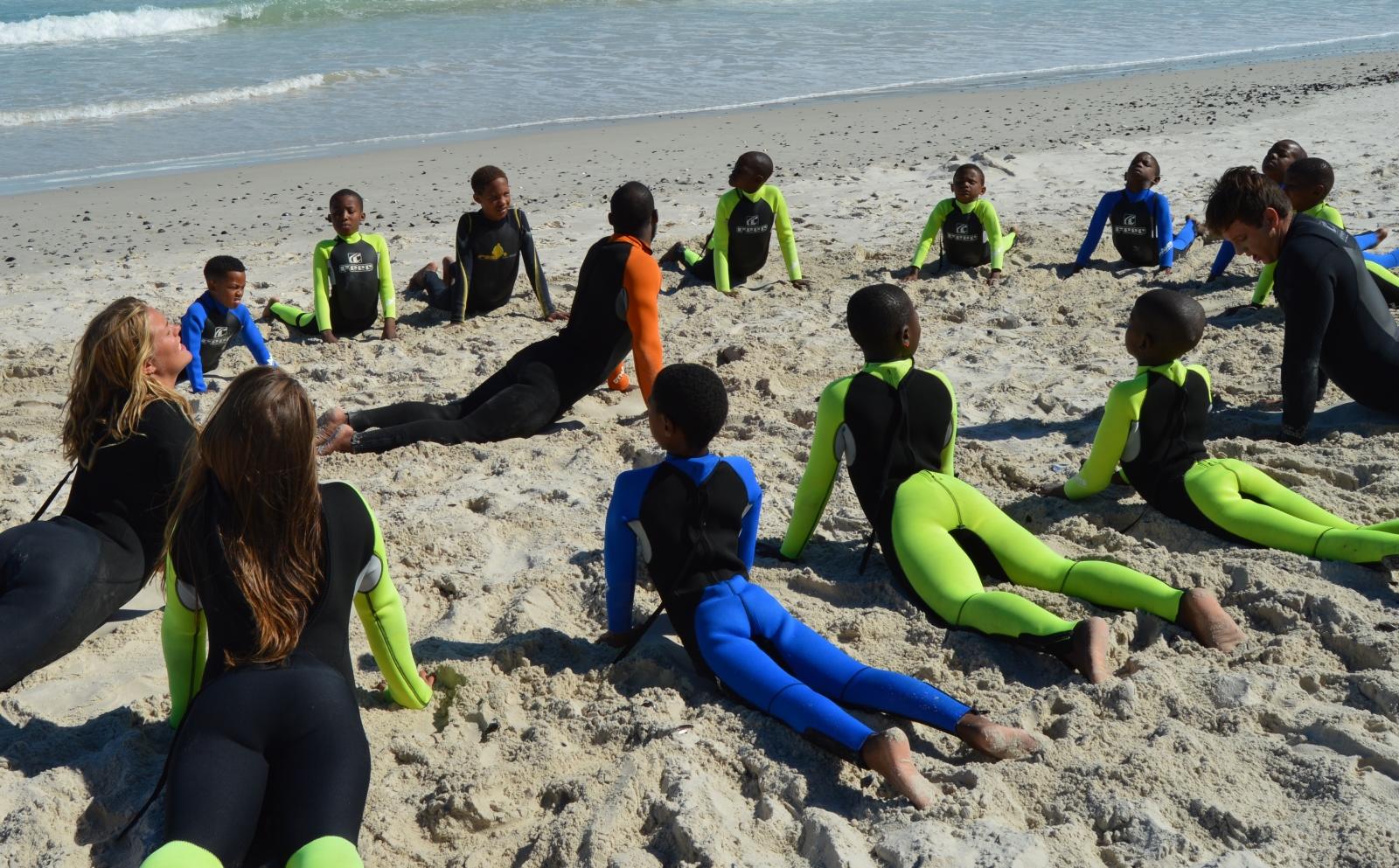 Volunteers and South African children stretch on a surfing program for last minute volunteering abroad.