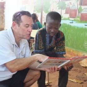 An older volunteer reads to a child as part of his childcare volunteer work overseas