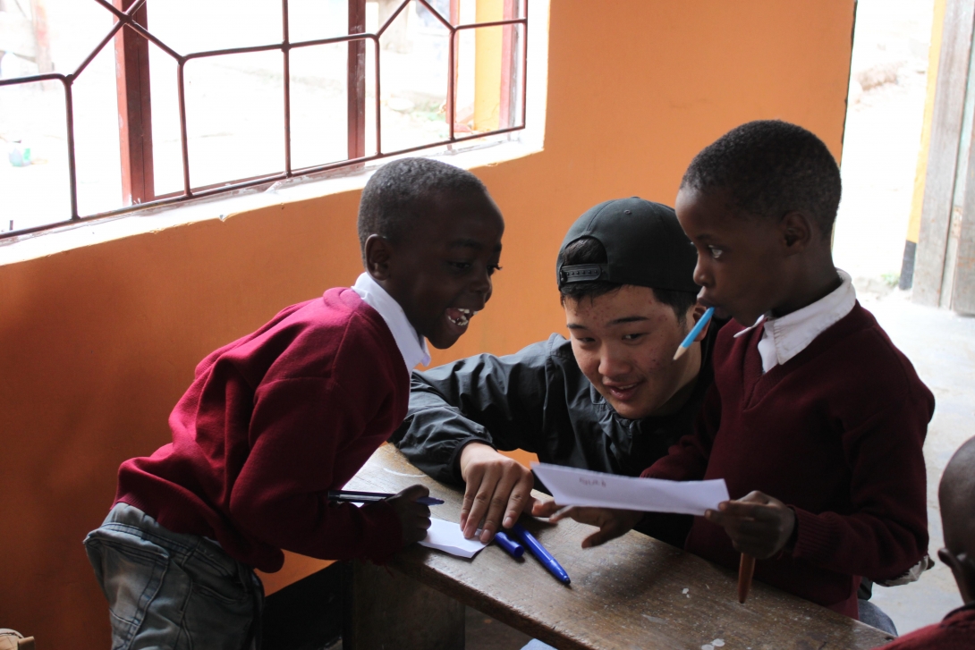 A high school students helping two children with basic English during his volunteering abroad trip