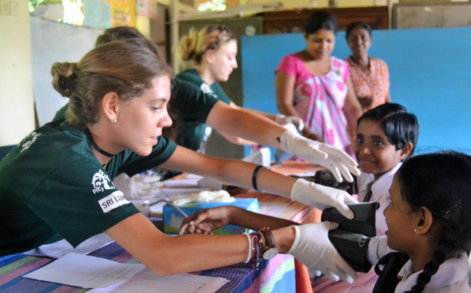 During her high school volunteer trip abroad, a Public Health volunteer measures blood pressure in a medical outreach.