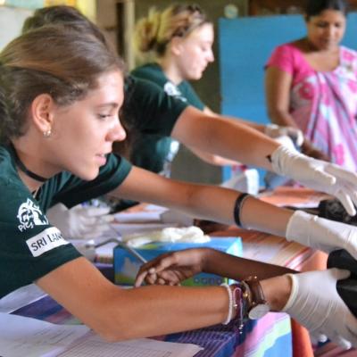 During her high school volunteer trip abroad, a Public Health volunteer measures blood pressure in a medical outreach.