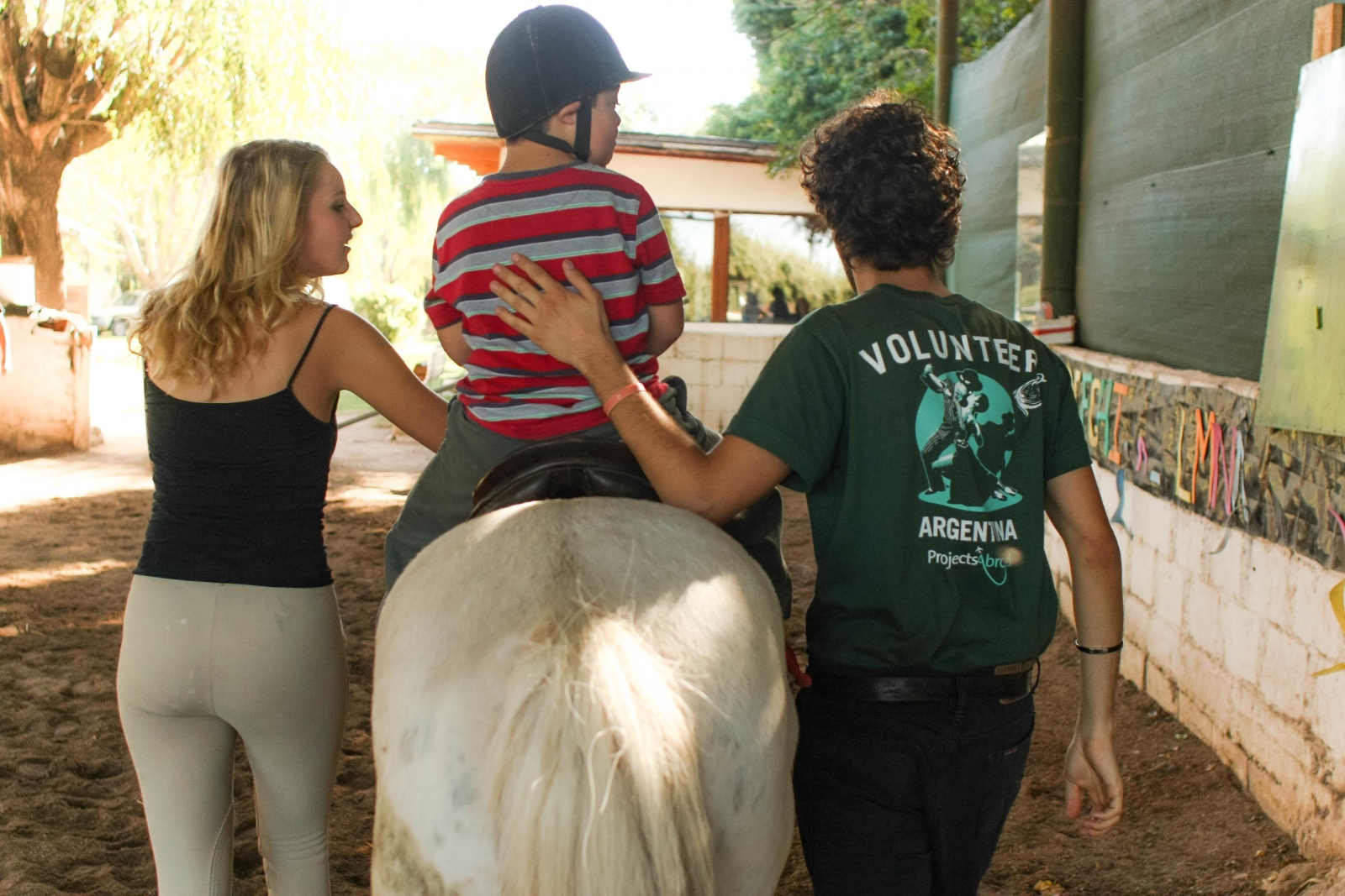 Volunteers in South America assist a young child with horse riding at our Equine Therapy Project in Argentina. 