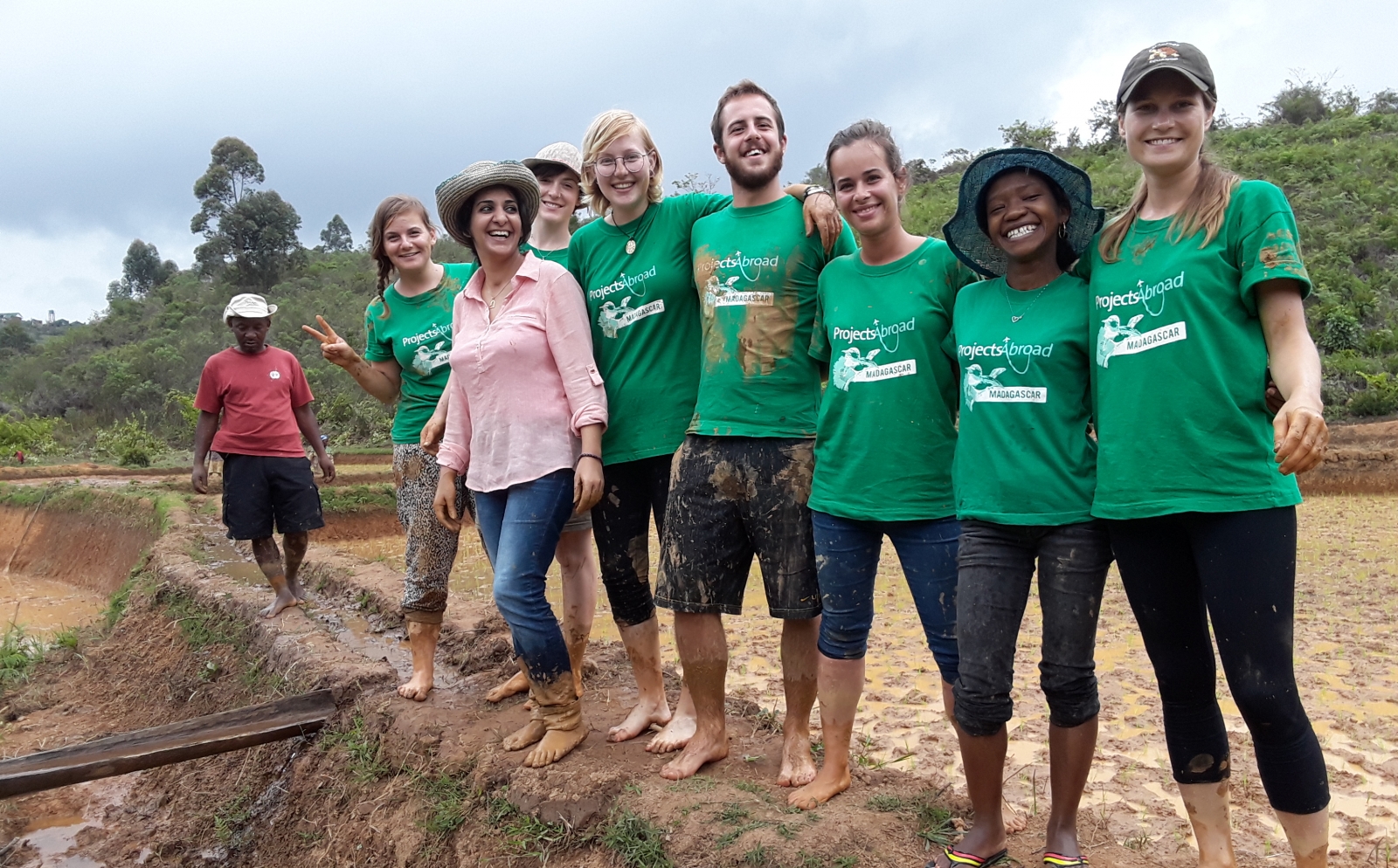 A group of muddy recent graduates take a break from planting rice in Madagascar during their volunteer abroad experience. 