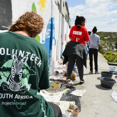 A volunteer paints a mural on a school wall during her volunteer work abroad