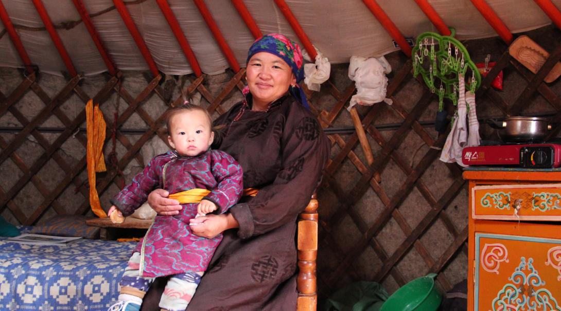 A Mongolian nomad woman and child sit in their ger