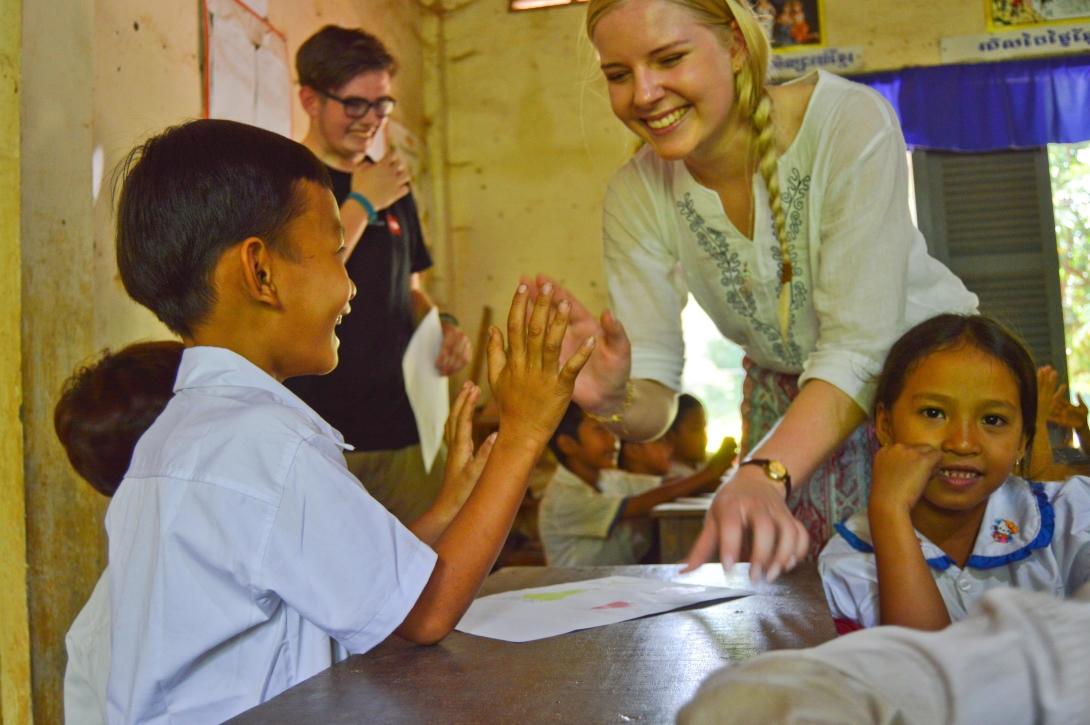 A high school volunteer plays a game with a young boy during her class in Cambodia