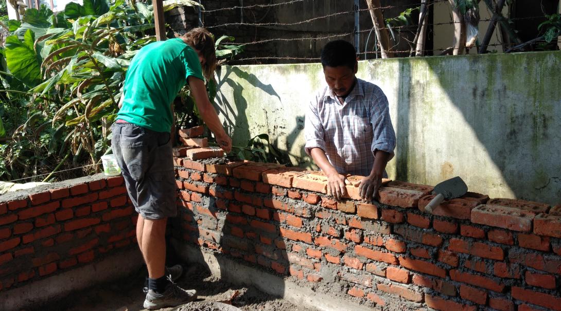 A volunteer is helping a local builder with building a wall during the Building Project in Nepal