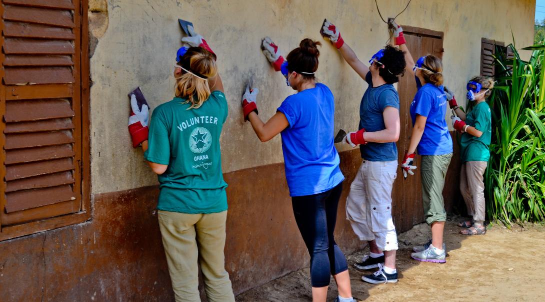 Construction volunteers in Ghana scraping off old paint from a wall.