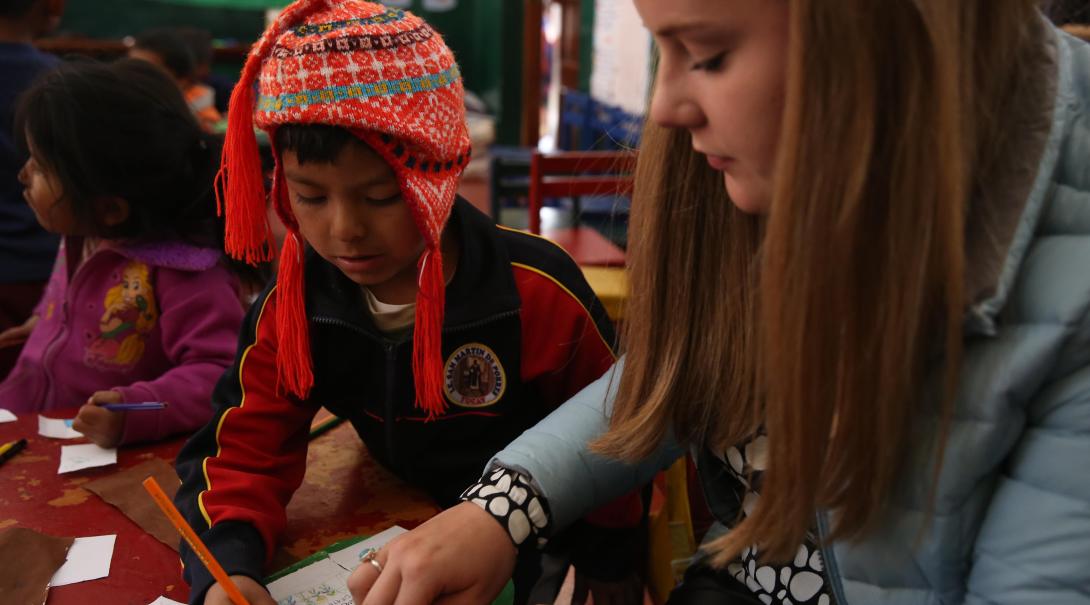 Childcare volunteer in Peru helps a kid during arts and crafts activity as part of her volunteer work for teenagers.