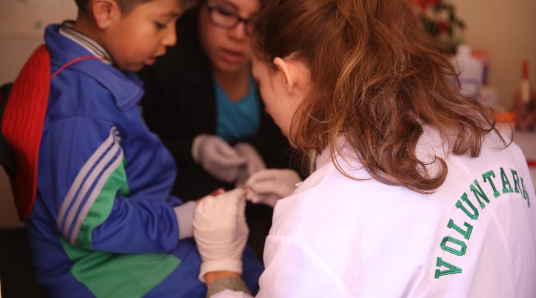 A high school student doing a summer medical internship abroad in Peru checks a child's blood sugar levels. 