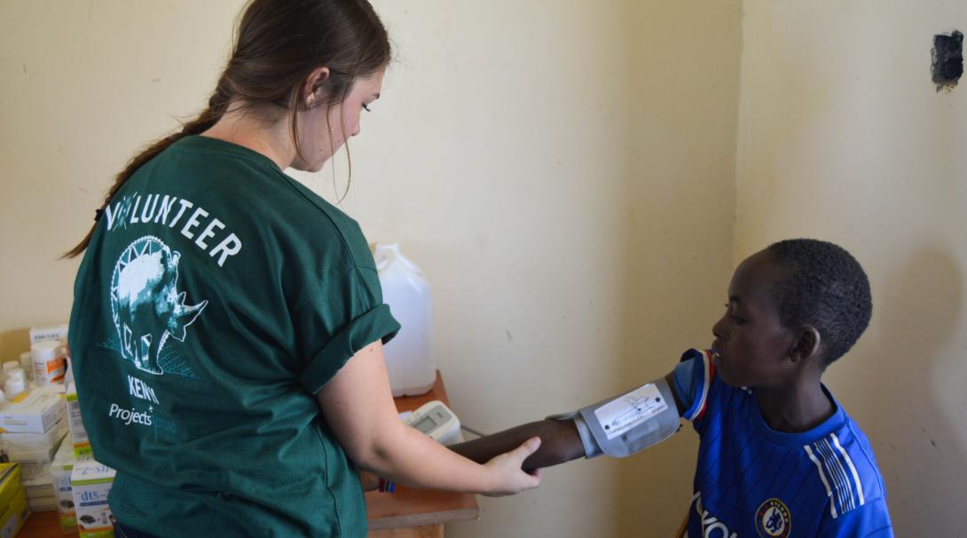 A teenage volunteer doing a medical internship with Projects Abroad in Kenya takes the blood pressure to a child.