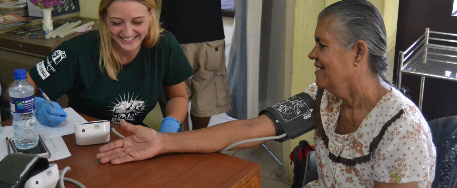 A student doing a medical internship for high school students in Sri Lanka checks blood pressure levels for a local woman.  