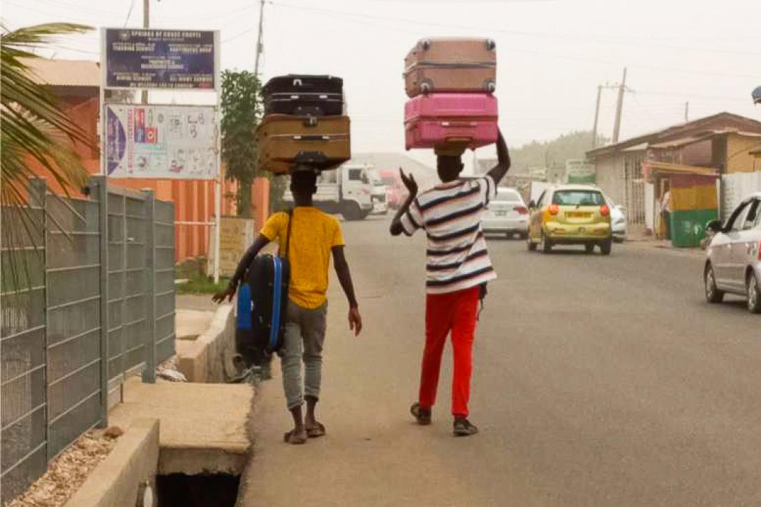 Two men in Ghana are carrying suitcases down the street using their heads