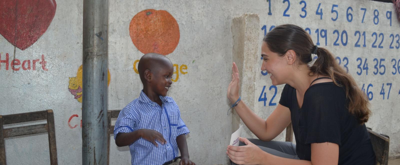 A Childcare volunteer in Ghana offers a child a high five for successfully completing an educational task. 